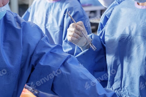 Preview: Surgeon holding needle driver with thread while preparing to close a wound in the operating room