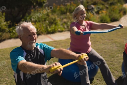 Preview: Front view of active senior man and woman exercising with elastic band and ball in park