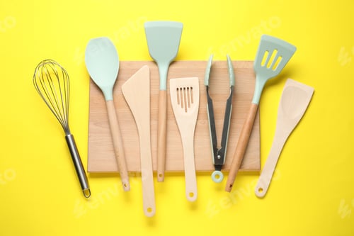 Preview: Different spatulas, whisk and tongs on yellow background, flat lay