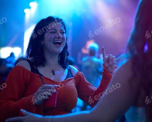 Preview: Two Female Friends Wearing Glitter Dancing At Outdoor Summer Music Festival Holding Drinks At Night