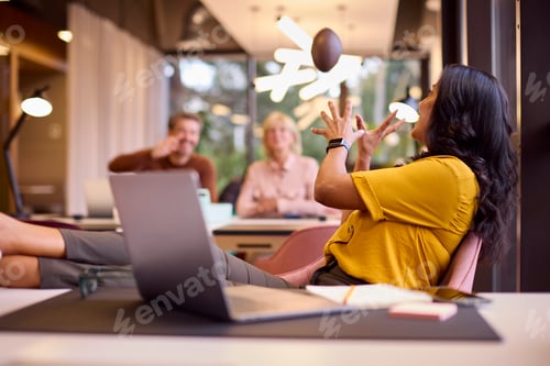 Preview: Mature Businesswoman With Feet On Desk In Office Catching Small American Football