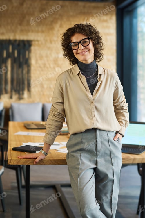 Preview: Smiling young female ceo of business company standing by workplace