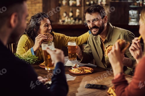 Preview: Group of happy friends having fun while drinking beer and eating hamburgers in a pub.