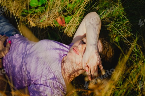 Preview: the girl lies in the grass, the bright rays of the sun fall on her face