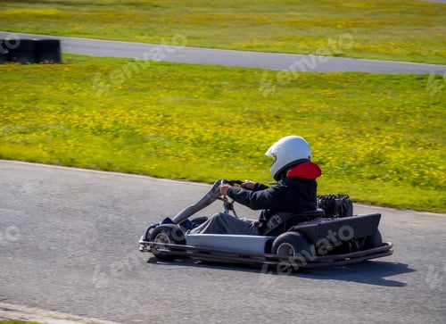 Preview: Go-cart racer with a white helmet on the circuit during daytime