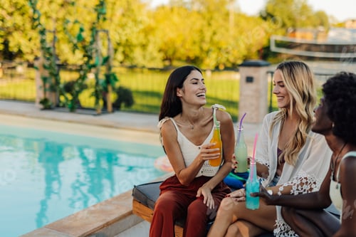 Preview: Three young women having fun drinking cocktails by the poolside