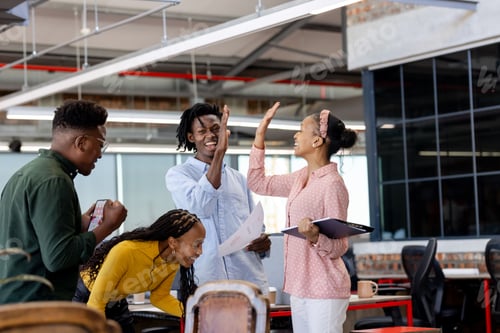 Preview: African American colleagues celebrating success with high five in modern office