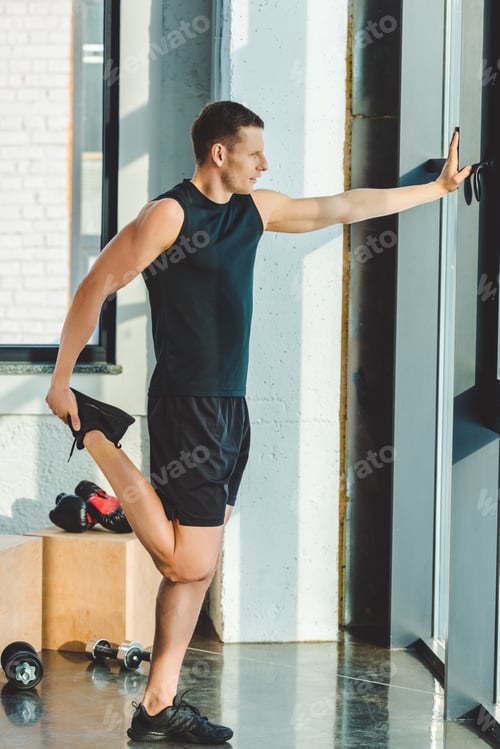 Preview: side view of young man stretching before workout in gym