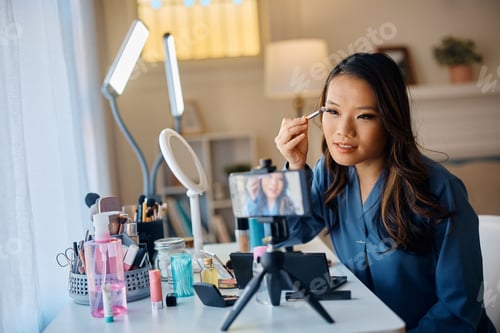 Preview: Asian makeup artist applying eyeshadow while recording beauty tutorial with smart phone.