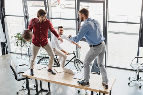 Preview: high angle view of young businessmen having fun with basketball ball in office