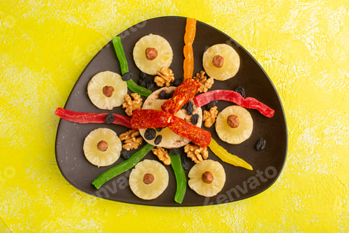 Preview: top view pineapple rings along with dried fruits and nougat inside brown plate on the yellow floor