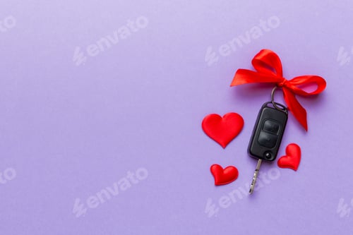 Preview: Car key with a red bow and a heart on Colored table. Giving present or gift for valentine day