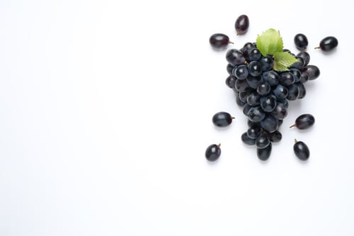 Preview: Bunch of dark blue grapes with leaves on white background, top view