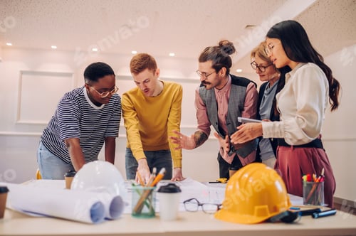 Preview: Multiracial team of architects having a meeting while using blueprints