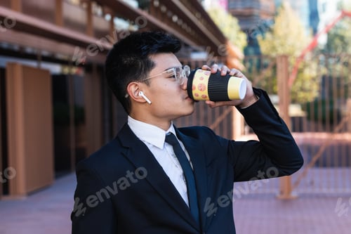 Preview: Asian businessman is drinking take away coffee outdoors in the city.