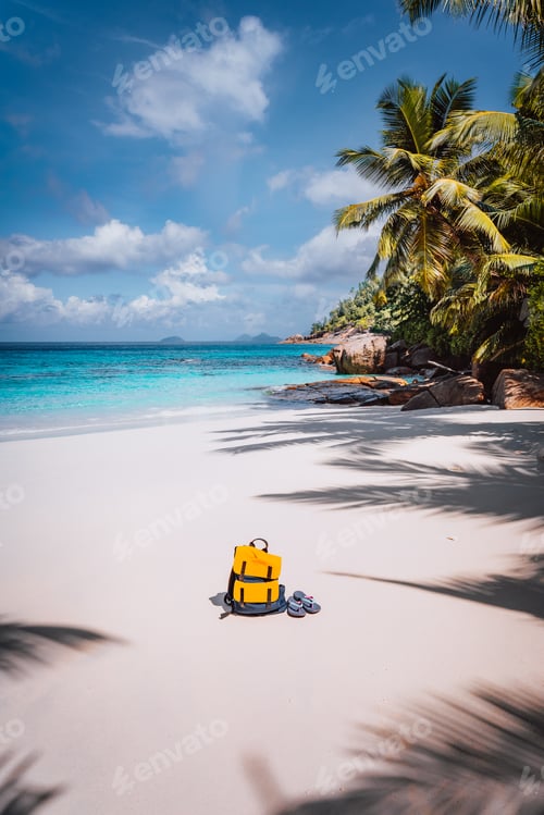 Preview: Yellow backpack and flip flops on beautiful tropical sandy beach. Palm trees and blue sky. Holiday