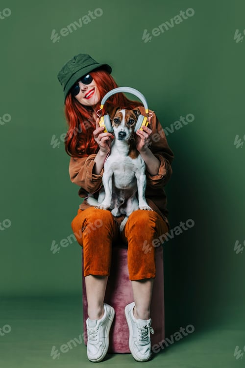Preview: Stylish redhead woman with headphones and dog on green background