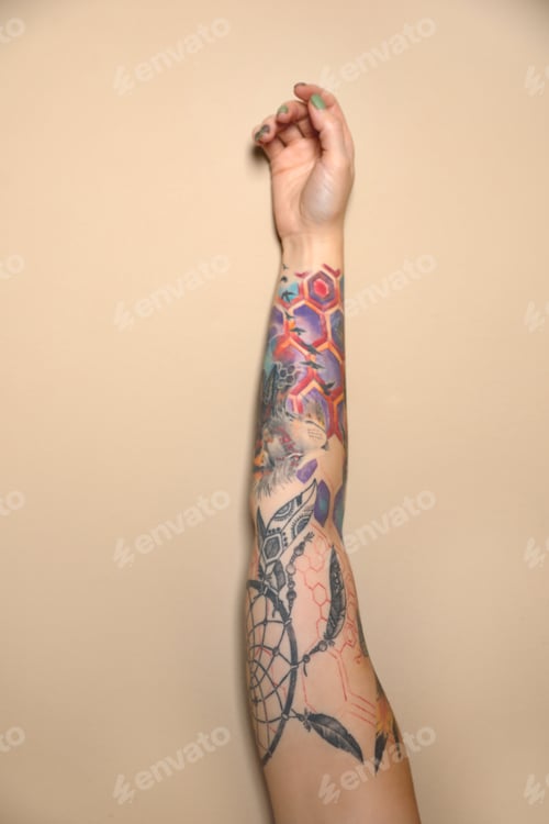 Preview: Woman with colorful tattoos on arm against beige background, closeup