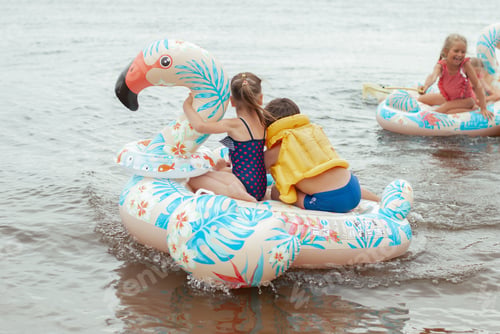 Preview: Happy kids swimming on the blown flamingo on the river water. Summer vacation