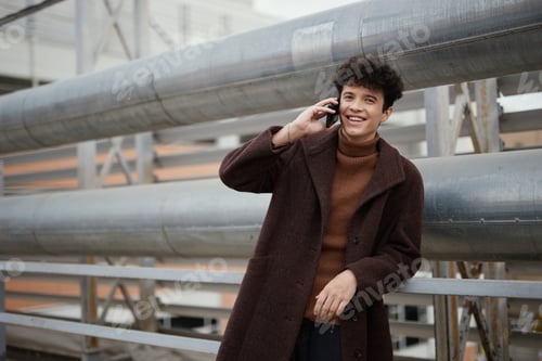 Preview: Fashionable man in a brown coat using a cell phone on a city street in front of a building with