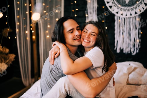 Preview: Young couple man woman sitting on the bed decorated with Christmas winter holidays garland lights
