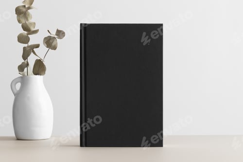 Preview: Black book mockup with eucalyptus decoration on a beige table.