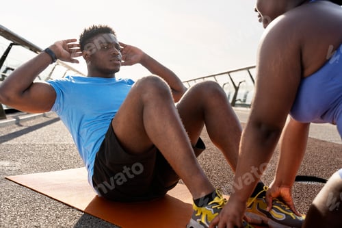 Preview: Portrait of attractive African American man exercising, do abs, sitting on yoga mat outdoors