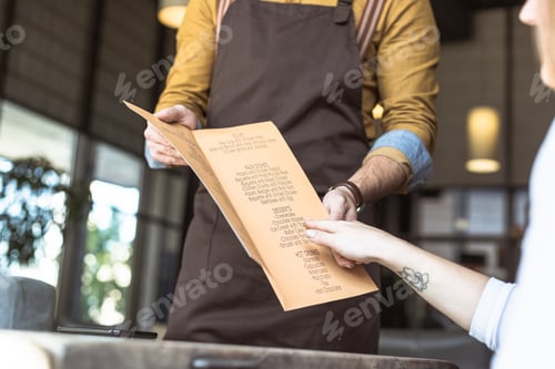 Preview: cropped shot of waiter showing menu list to female customer in cafe