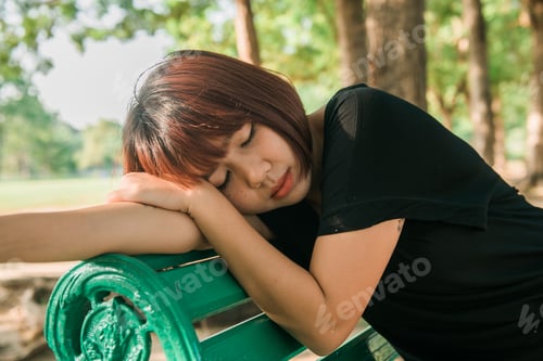 Preview: Young Asian woman sitting outdoor on the public bench and lying along the bench in the park.