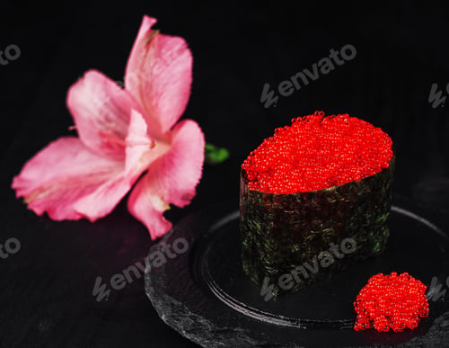 Preview: Gunkan maki sushi with red caviar tobiko and pink flower resting on black slate plate