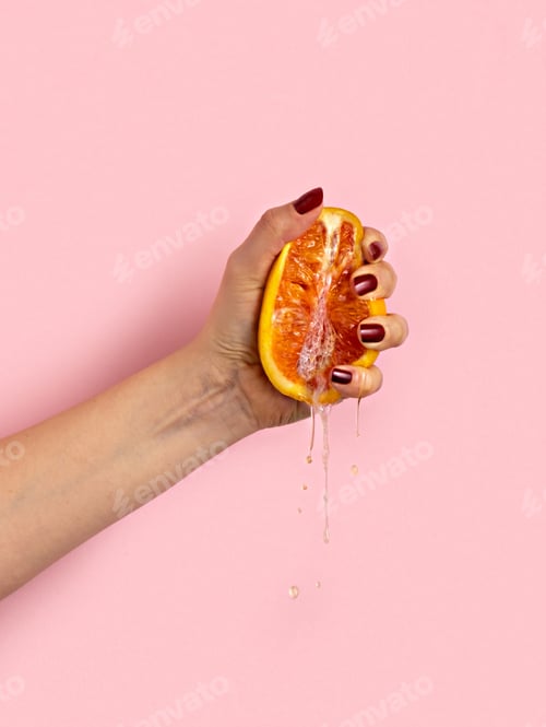 Preview: Female hand with half of juicy orange on pink background. Sex concept.