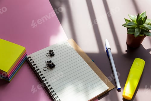 Preview: Top view shot of a notebook, sticky paper, pen, and a highlighter on a pink and brown background