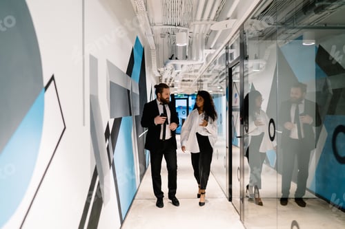 Preview: Business people discussing in office corridor while standing near glass wall