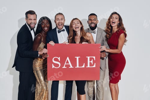 Preview: Group of beautiful people in formalwear holding sale banner and smiling