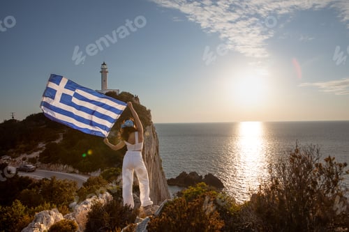Preview: woman with greece flag looking at sunset above the sea