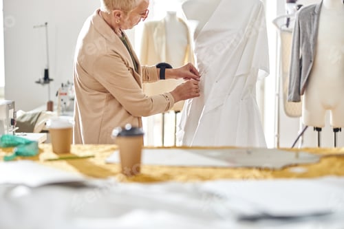 Preview: Mature seamstress pins fabric gathers making new dress on mannequin in studio