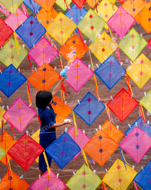 Preview: Vertical image of Asian girl enjoy to play bubble gun alone in area of row of kites outdoor