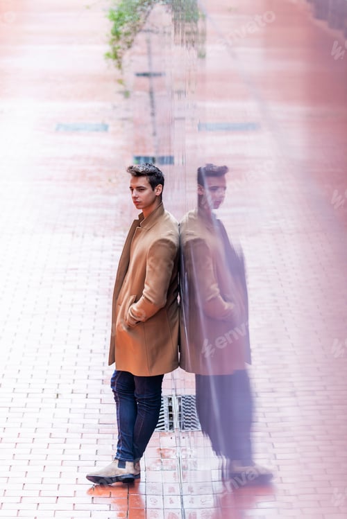 Preview: Portrait of stylish handsome young man with coat standing outdoors and leaning on wall.