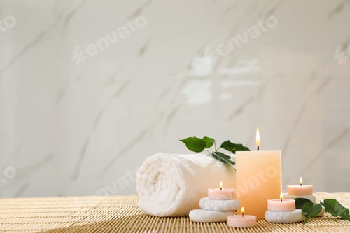 Preview: Composition of spa stones, towel and burning candles on bamboo mat, space for text
