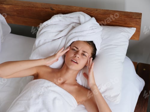 Preview: A woman lies on a bed in the morning on a pillow under a blanket in the bedroom after a shower in a