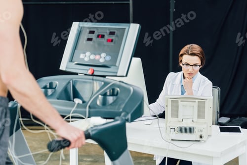 Preview: doctor at desk conducting endurance test with sportsman in gym