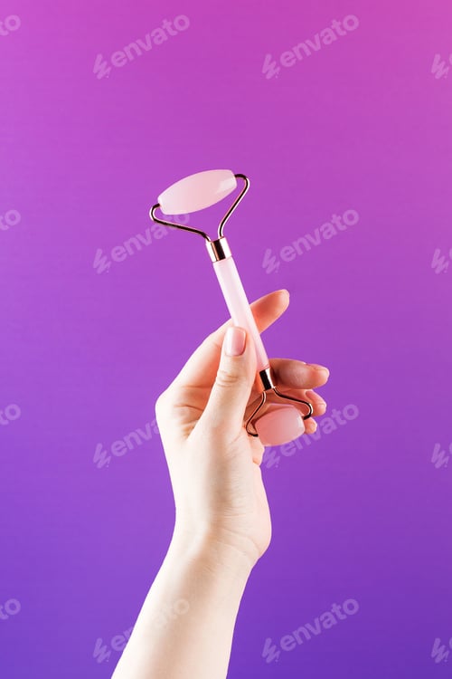 Preview: Woman shows quartz face roller antiaging massaging tool natural stone on purple
