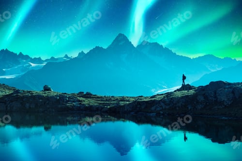 Preview: Tourist on mountain lake during incredible Aurora borealis Northern lights