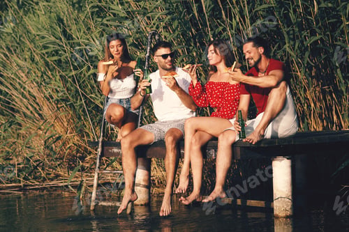 Preview: Group of young people enjoy a summer day by the river eating pizza and drink beer