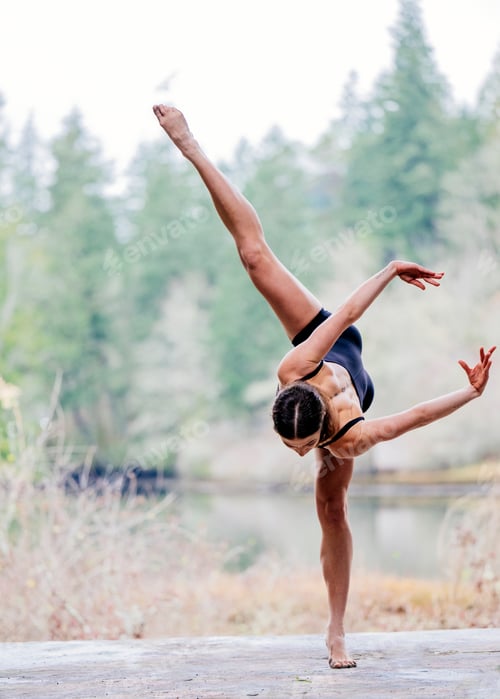 Preview: Dancer performs a high arabesque outdoors by a tranquil forest lake. USA