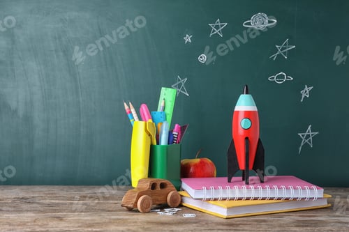 Preview: Bright toy rocket and school supplies on wooden desk. Space for text