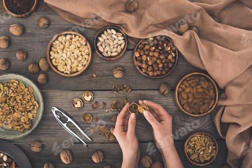 Preview: top view of person cracking walnut above wooden table