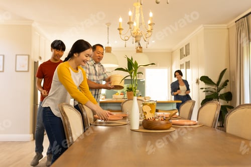 Vista previa: Setting dining table, multiracial family preparing for meal together in cozy home dining room