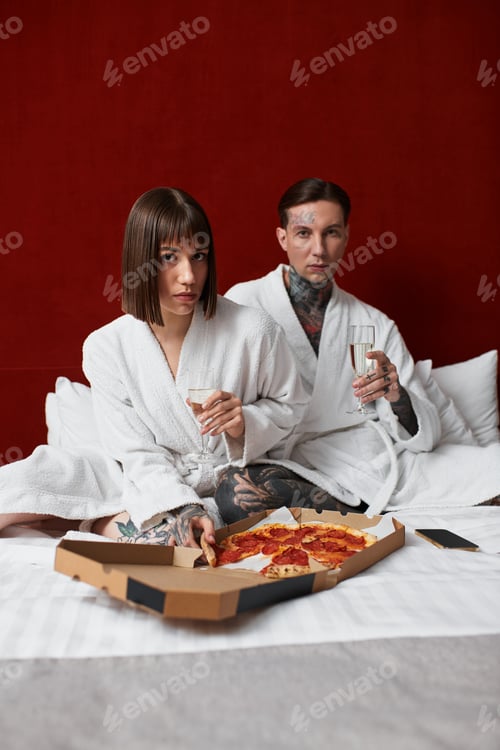Preview: Young couple shares a cozy evening in their hotel room with pizza and champagne