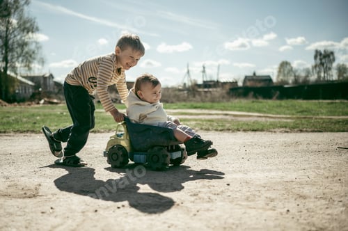 Preview: The boy rides his younger brother's toy car. Summer in the village